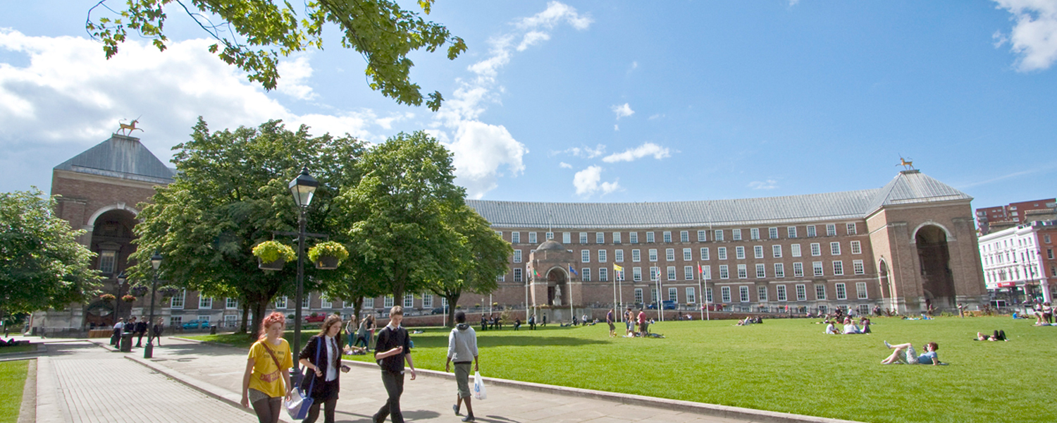 a group of young people walking along college green with city hall in the background