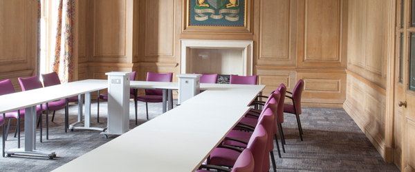 a large wood panelled room with a long rectangular table and red chairs