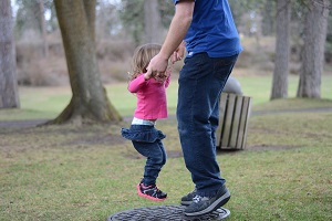 An adult and small child holding hands and jumping happily in a park