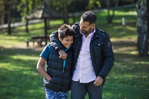 A man with his arm around the shoulders of a teenage boy, laughing