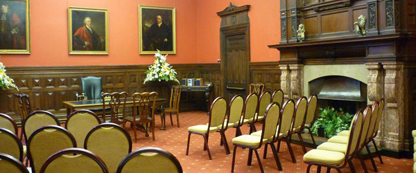 a heritage room with a rectangular antique table, rows of chairs, and large paintings on the walls